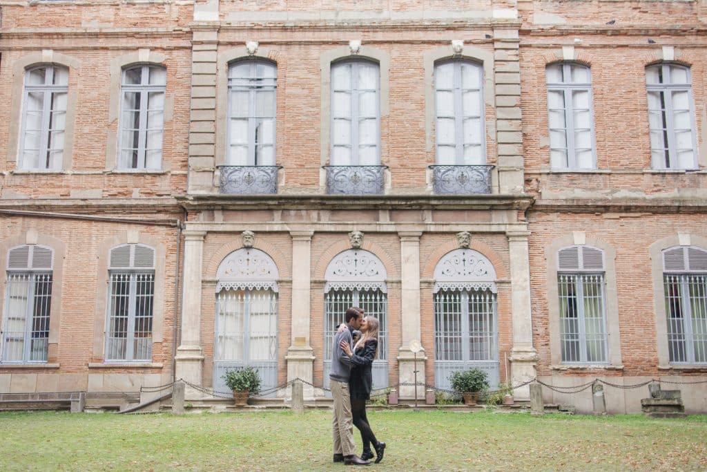 un couple qui se fait un bisous devant un grand batiment en briques