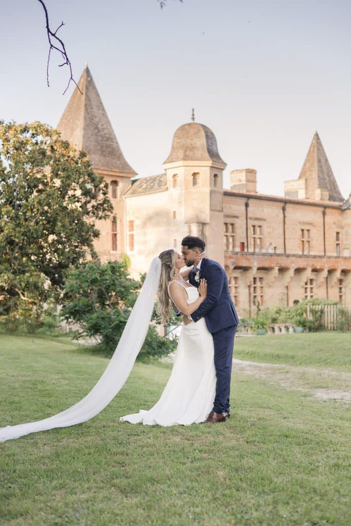 un couple de mari&eacute;s devant un magnifique chateau se font un bisous avec une posture un peu panch&eacute;e