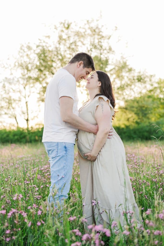 un couple au milieu de champs de fleurs avec le coucher de soleil derri&egrave;re, se touche les fronts, la femme est enceinte